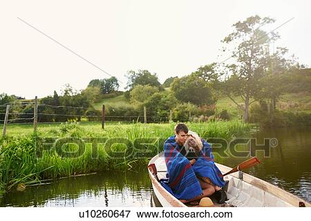 Stock Photo - Young couple wrapped and huddled in blanket in river rowing boat. Fotosearch