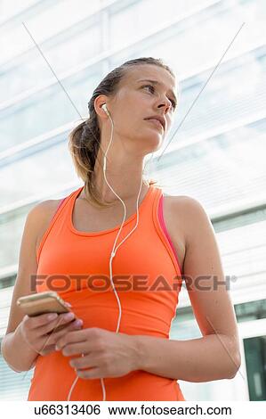 Stock Photograph - Young female runner wearing earphones in city. Fotosearch