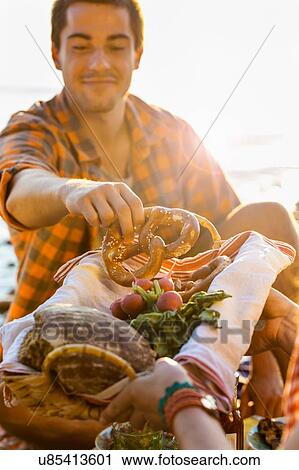 Young man accepting pretzel from bread basket, looking down smiling View Large Photo Image Stock Image - Young man accepting pretzel from bread basket, looking down smiling. Fotosearch