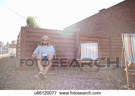 Young man alone on deckchair at rooftop party View Large Photo Image Stock Photo - Young man alone on deckchair at rooftop party. Fotosearch