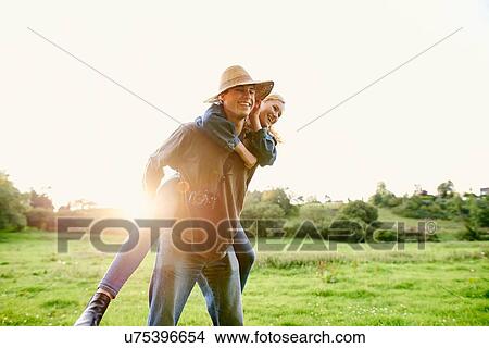 Young man giving girlfriend a piggyback in rural field View Large Photo Image Picture - Young man giving girlfriend a piggyback in rural field. Fotosearch