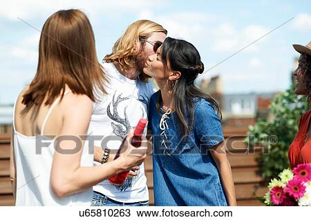 Stock Image - Young man greeting female friends at rooftop party. Fotosearch