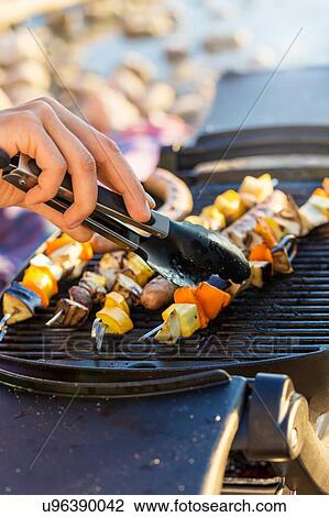Young mans hand using tongs to turn sausages and kekabs on barbecue griddle View Large Photo Image Stock Image - Young mans hand using tongs to turn sausages and kekabs on barbecue griddle. Fotosearch