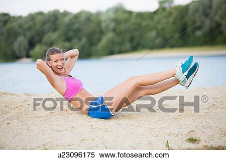 Stock Photography - Young woman doing warm up exercises at lakeside. Fotosearch
