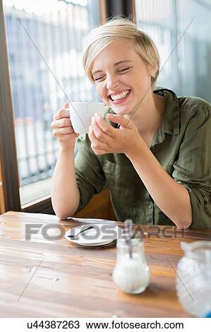 Stock Image - Young woman drinking coffee at cafe table. Fotosearch