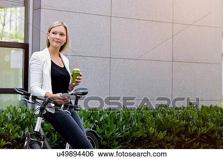 Stock Photograph - Young woman leaning against bicycle using smartphone. Fotosearch