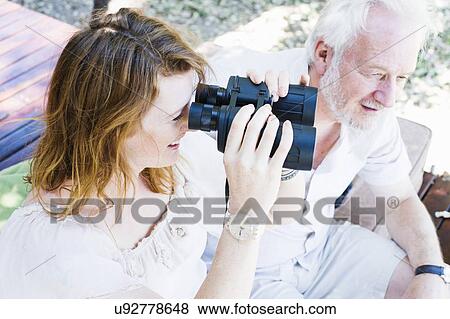 Stock Photo - Young woman looking out through binoculars from safari lodge, Kafue National Park, Zambia. Fotosearch