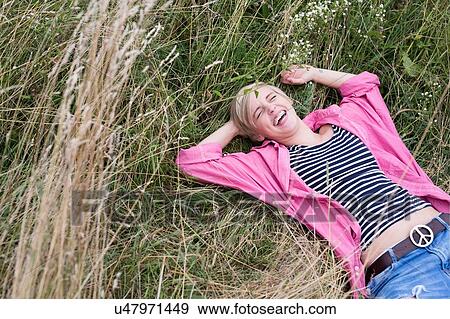 Stock Photo - Young woman lying in long grass laughing. Fotosearch