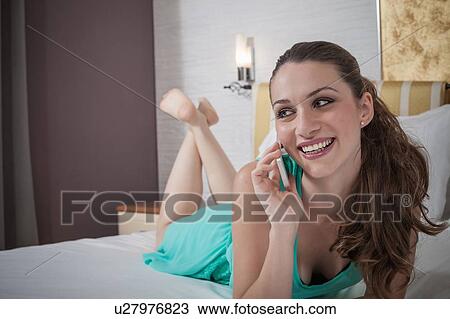 Young woman lying on hotel bed chatting on smartphone View Large Photo Image Stock Image - Young woman lying on hotel bed chatting on smartphone. Fotosearch