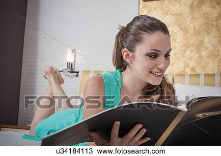 Young woman lying on hotel bed reading menu View Large Photo Image Stock Image - Young woman lying on hotel bed reading menu. Fotosearch