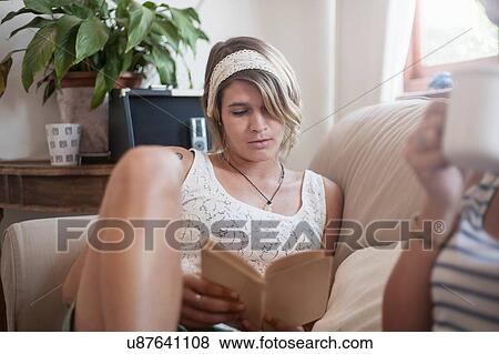 Stock Photo - Young woman relaxing on sofa, reading book. Fotosearch