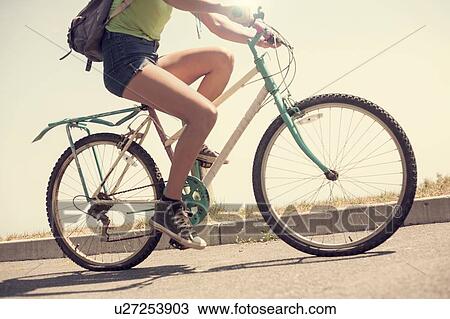 Stock Image - Young woman riding bicycle, low section. Fotosearch