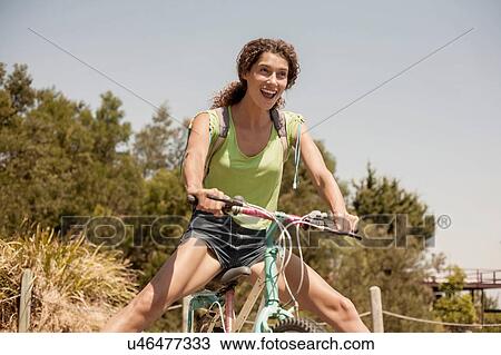 Stock Image - Young woman riding bicycle, outdoors, smiling. Fotosearch