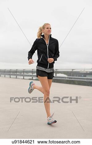 Stock Image - Young woman running, outdoors. Fotosearch