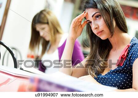 Young woman sitting at desk, studying, pensive expression View Large Photo Image Stock Photo - Young woman sitting at desk, studying, pensive expression. Fotosearch