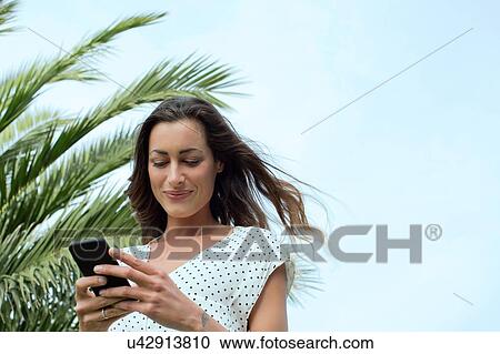 Stock Image - Young woman texting on smartphone. Fotosearch