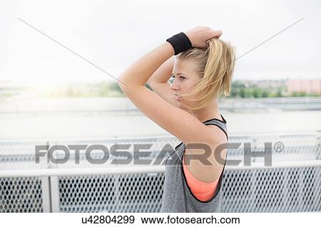 Young woman tying hair, preparing for workout, outdoors View Large Photo Image Stock Photo - Young woman tying hair, preparing for workout, outdoors. Fotosearch