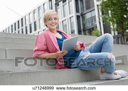 Young woman using digital tablet on city stairway View Large Photo Image Stock Photo - Young woman using digital tablet on city stairway. Fotosearch