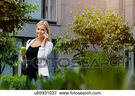 Stock Photo - Young woman walking and talking on smartphone. Fotosearch