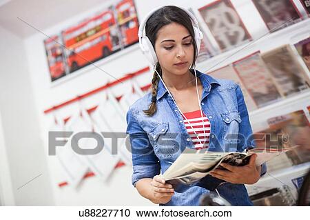 Young woman wearing headphones, looking through magazine, indoors View Large Photo Image Stock Image - Young woman wearing headphones, looking through magazine, indoors. Fotosearch