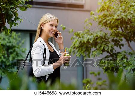 Young woman with smoothie drink walking and talking on smartphone View Large Photo Image Stock Photo - Young woman with smoothie drink walking and talking on smartphone. Fotosearch