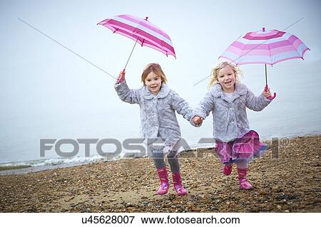 Stock Photo - MODEL RELEASED. Two girls on the beach holding umbrellas.. Fotosearch
