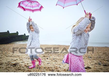 Stock Photograph - MODEL RELEASED. Two girls on the beach holding umbrellas.. Fotosearch
