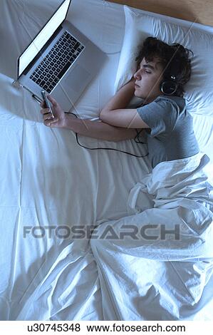 Stock Photo - MODEL RELEASED. Young man asleep in bed with laptop and phone.. Fotosearch