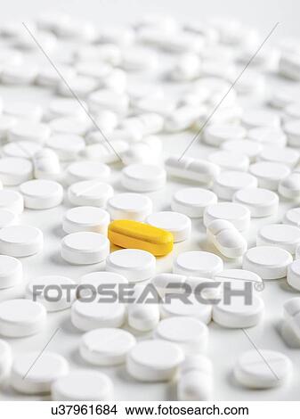 Stock Illustration - White tablets with a yellow capsule, close up.. Fotosearch