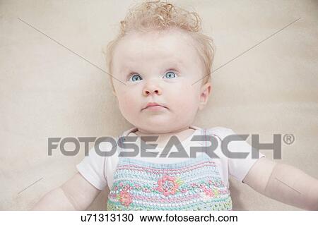 Stock Image - Baby girl lying down, looking away. Fotosearch