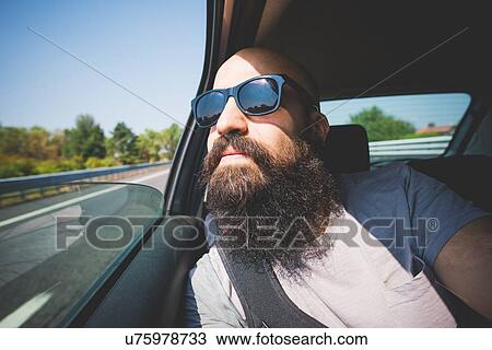 Stock Image - Bearded man looking out of car window on highway, Garda, Italy. Fotosearch