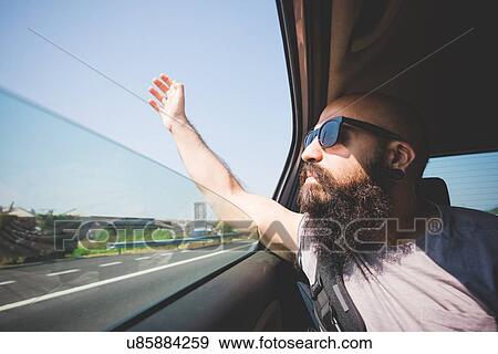 Stock Photo - Bearded man sticking hand out of car window on highway, Garda, Italy. Fotosearch