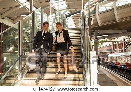 Stock Photo - Businessman and businesswoman coming down stairs, Underground station, London, UK. Fotosearch