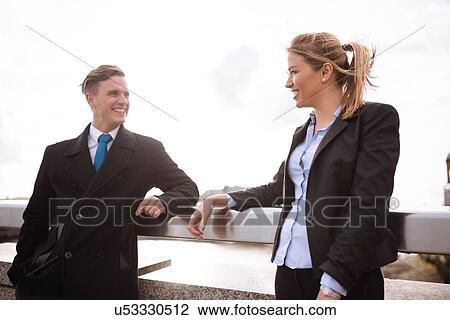Stock Image - Businessman and businesswoman leaning on rail. Fotosearch