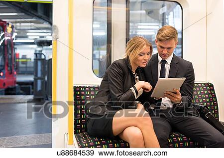 Stock Photo - Businessman and businesswoman sharing digital tablet, London Underground, UK. Fotosearch