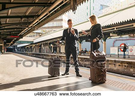 Stock Image - Businessman and businesswoman texting on platform, Underground station, London, UK. Fotosearch