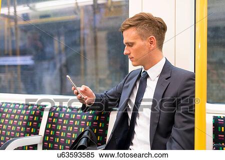 Stock Photography - Businessman texting on tube, London Underground, UK. Fotosearch
