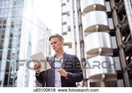Stock Photo - Businessman using digital tablet in street, London, UK. Fotosearch
