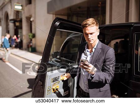 Businessman using smartphone while exiting black cab, London, UK View Large Photo Image Stock Photo - Businessman using smartphone while exiting black cab, London, UK. Fotosearch