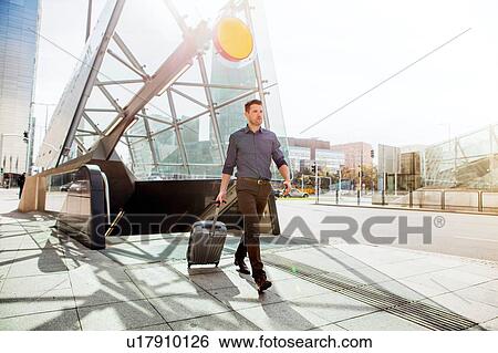 Stock Photograph - Businessman with wheeled suitcase by escalator. Fotosearch