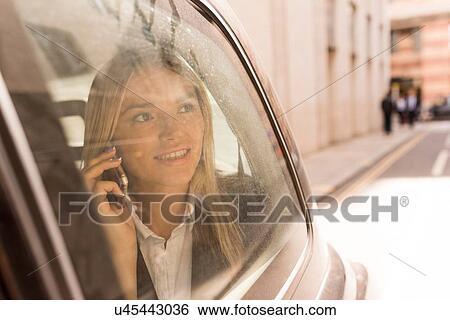 Stock Photograph - Businesswoman looking out of black cab, London, UK. Fotosearch
