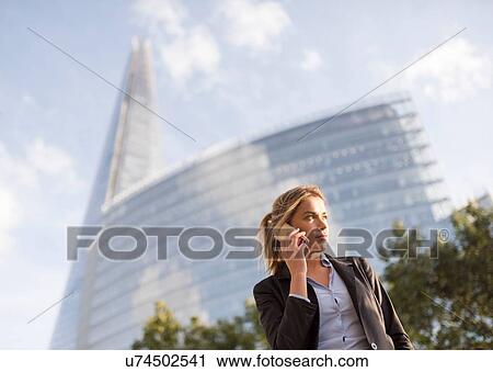 Stock Image - Businesswoman making call, buildings in background, London, UK. Fotosearch