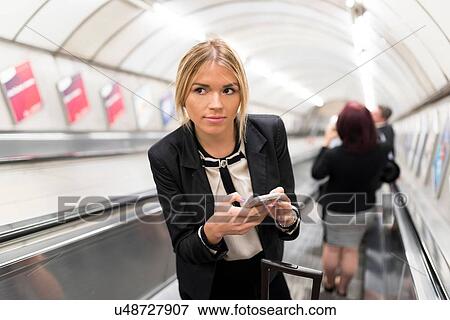 Stock Photo - Businesswoman texting on escalator, London Underground, UK. Fotosearch