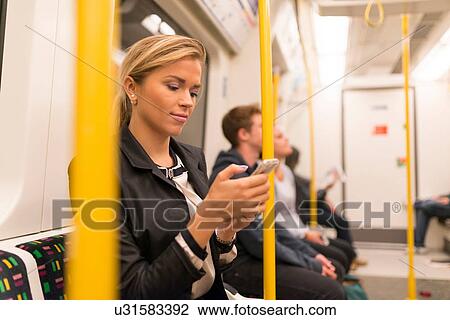 Stock Image - Businesswoman texting on tube, London Underground, UK. Fotosearch