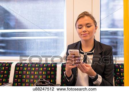 Stock Image - Businesswoman texting on tube, London Underground, UK. Fotosearch