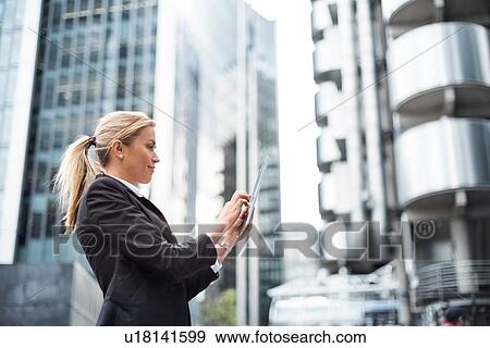 Stock Photo - Businesswoman using digital tablet in street, London, UK. Fotosearch