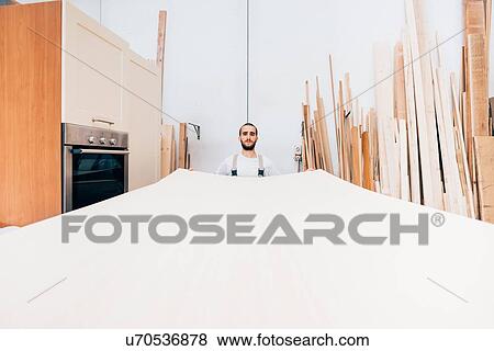 Stock Photo - Carpenter with large sheet of wood in workshop. Fotosearch