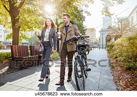 Casual businessman and woman pushing bike through park View Large Photo Image Stock Image - Casual businessman and woman pushing bike through park. Fotosearch