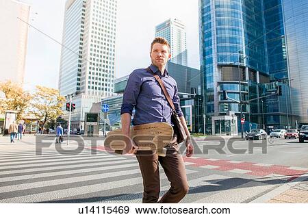 Stock Photo - Casual businessman crossing road holding skateboard. Fotosearch