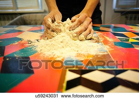 Stock Image - Close up of womans hands shaping dough on kitchen table. Fotosearch